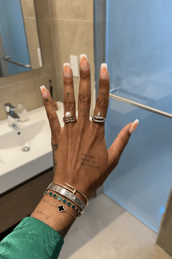 Orange aura French tips with gold details on a hand model