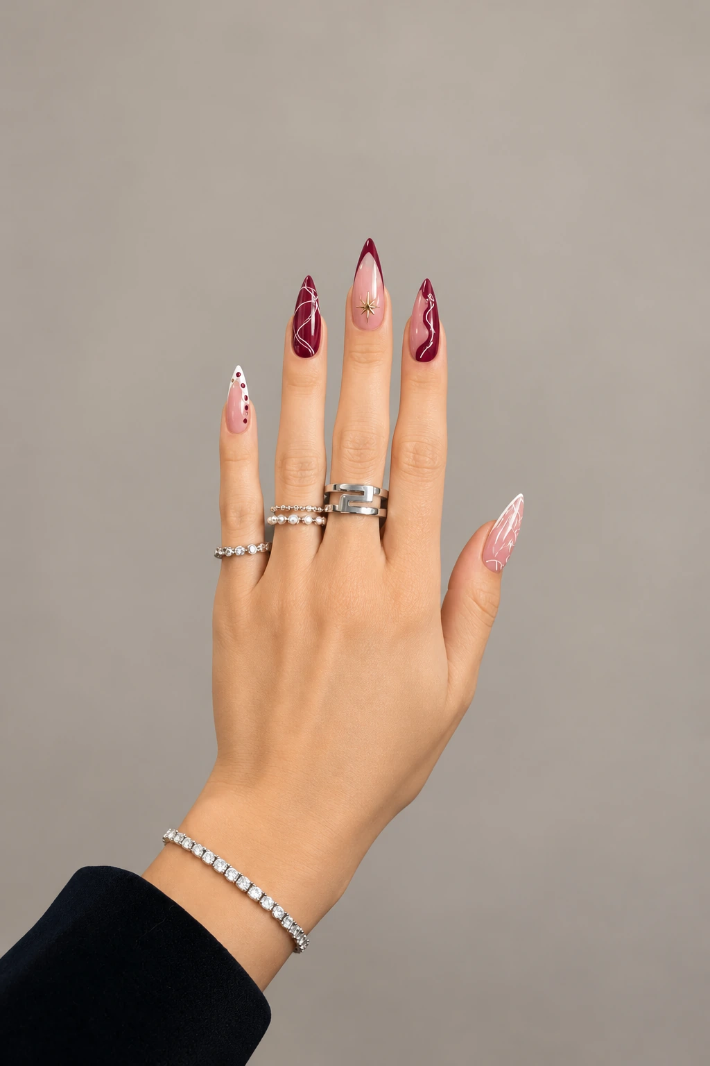 The same hand with long stiletto nails in sheer pink and burgundy, with white swirls, dots and a gold star against a soft neutral background